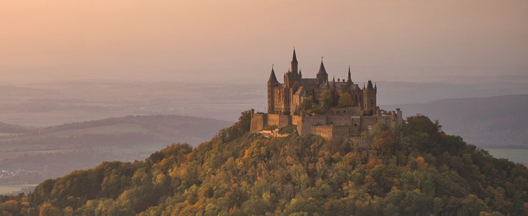 Burg Hohenzollern im Abendlicht über den Wäldern des Zollernalbkreises